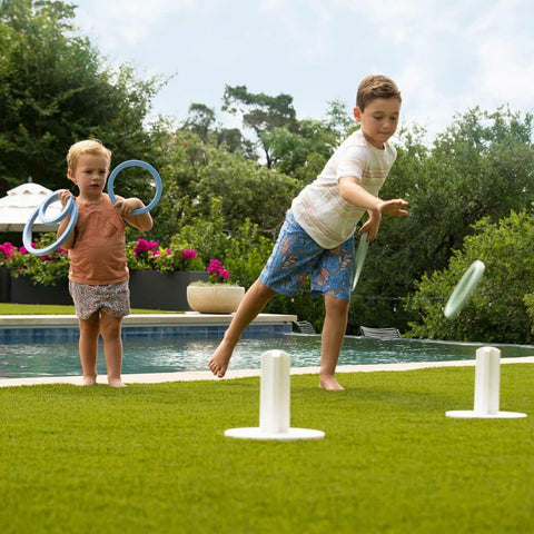 Two young children playing ring toss on the grass next to a pool