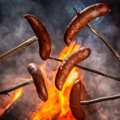 Five bratwursts on sticks in front of fire