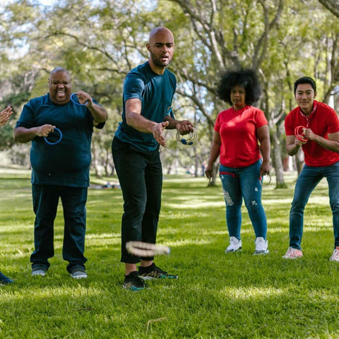 Four adults, two in teal shirts and two in red shirts, playing ring toss on grass