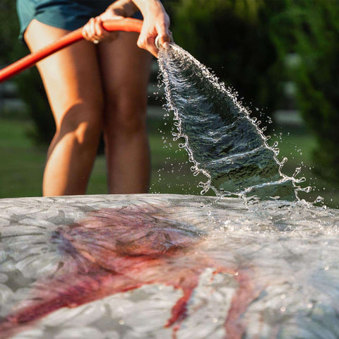 A woman hosing down wine stains off a Ledge Lounger Laze Pillow.