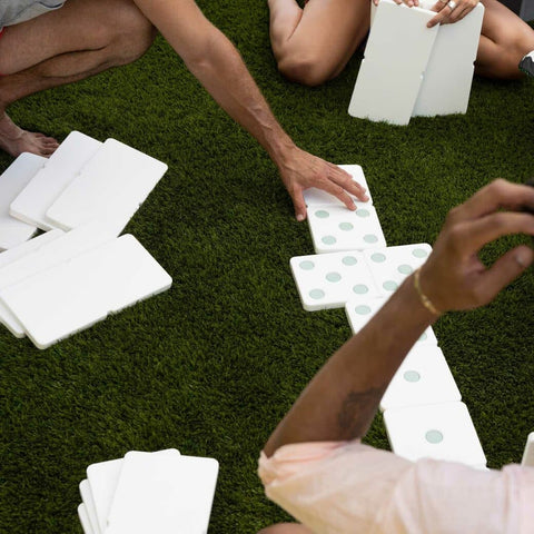 Three adults' arms playing with dominoes on grass