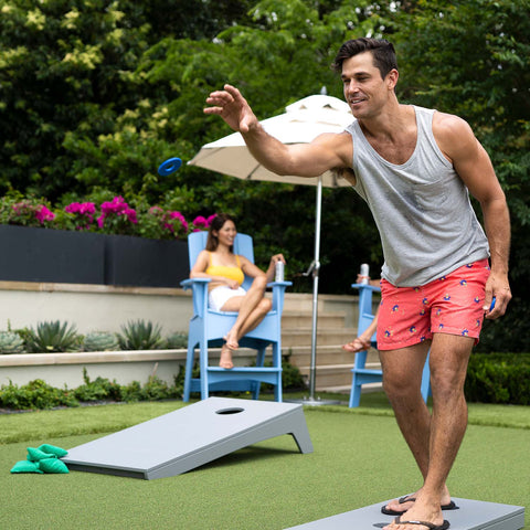 Outdoor game day, man tossing washer with corn hole in the background