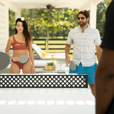 Couple in bathing suits playing ping pong under backyard pergola