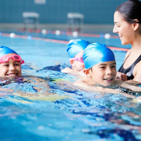 Children in swim caps being guided in pool by adult