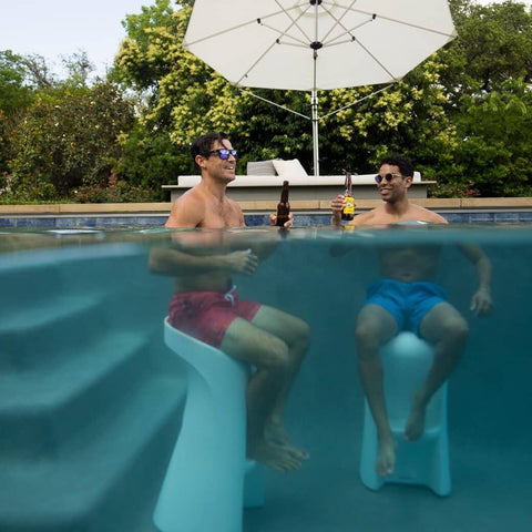 Two men holding beer bottles while sitting on Ledge Lounger in-pool barstools