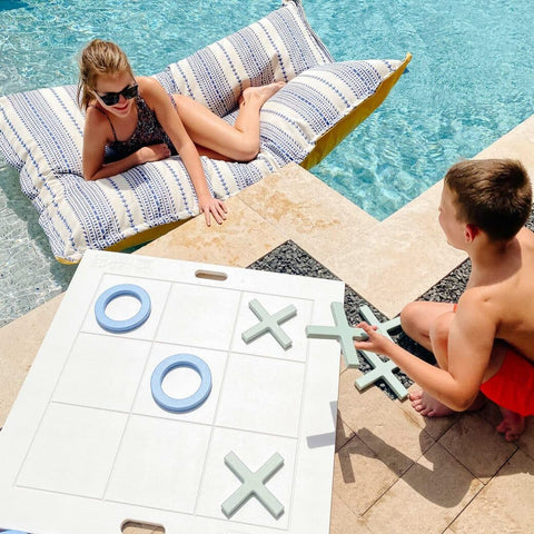 Person laying on Laze Pillow in pool playing Tic Tac Toe with child sitting next to pool