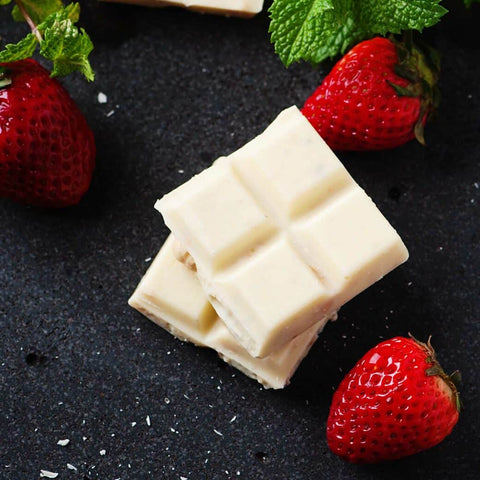 Two squares of white chocolate stacked on top of one another with three strawberries around it on a black background