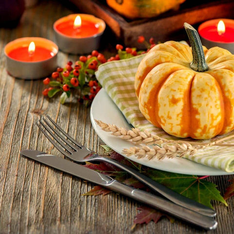 Autumn themed table setting with gourd, red candles and oranges on a natural wood table