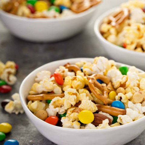 Three white bowls of popcorn with pretzels and M&M candy