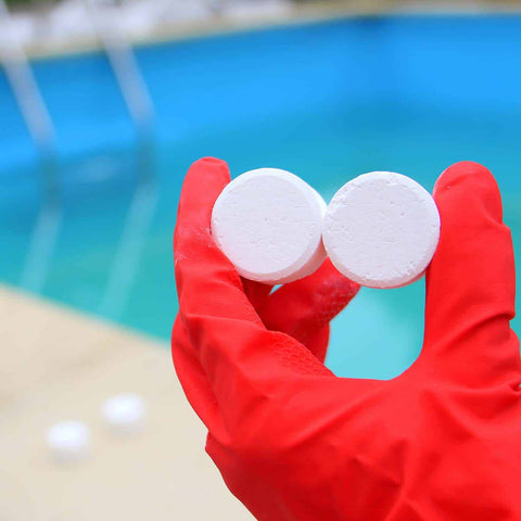Gloved hand holding chlorine tablets for cleaning the pool