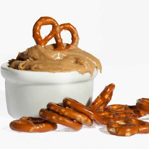 White ramekin filled with peanut butter with a pretzel on top, with pretzels all around it