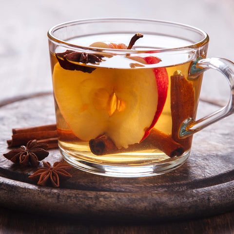 Spiced apple cider in a clear glass with piece of apple, cloves, and cinnamon