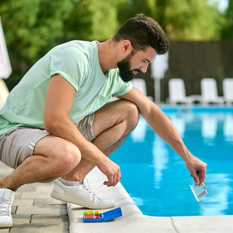Man kneeling at pool edge putting cleaner in water