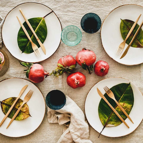 Tropical themed table setting with white plates, palm leaves and tropical fruit in center of table