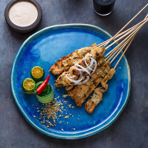 Chicken satay skewers on a blue plate