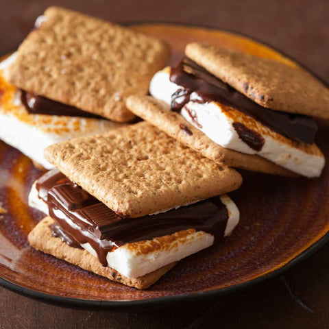 Three classic s'mores with graham crackers, toasted marshmallows, and melted chocolate sit on a brown ceramic plate