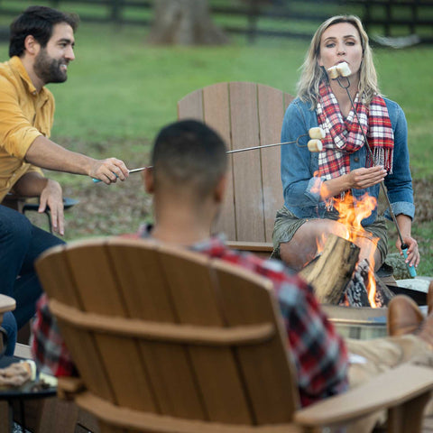 Friends sitting on Adirondack chairs around a fire, roasting marshmallows