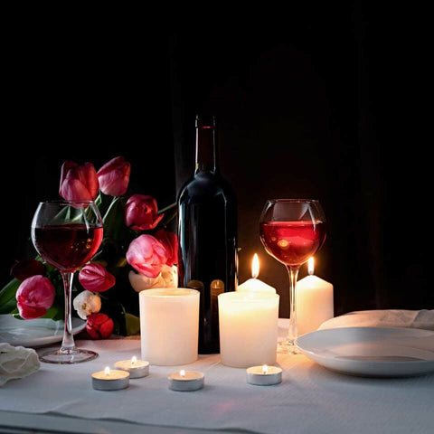 Romantic table setting with red wine, red roses and candlelight on black background
