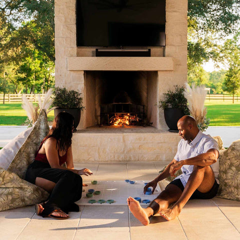 Couple playing tic tac toe on Laze Pillows by outdoor fireplace