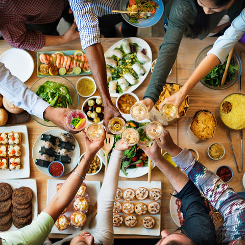 Clinking glasses over a table filled with finger foods at an outdoor party