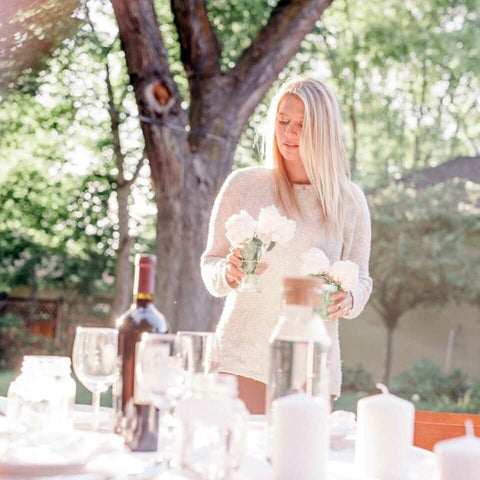 Table set with wine glasses and bottle of wine with woman about to place flowers in table