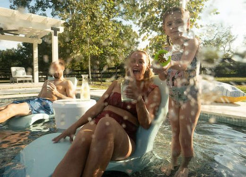 a woman sitting in a pool getting splashed by a little girl