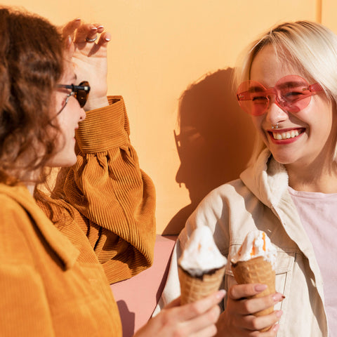 Women wearing sunglasses and holding ice cream smiling at each other
