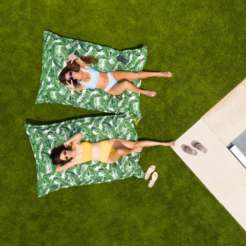 Women laying on Bold Jungle Laze Pillows by Ledge on the lawn