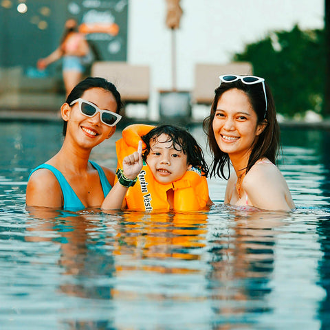 Kid wearing a life vest in pool with two women