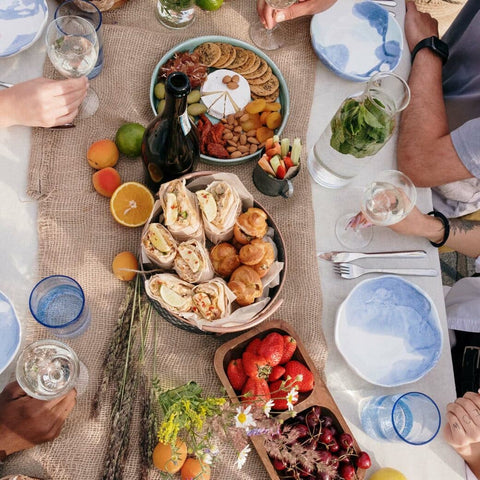 Overhead shot of brunch spread on burlap table runner, with people holding drinks on table