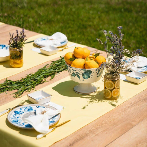 Wooden table set with yellow table runner, decorated plates, a decorated bowl of lemons, and foliage