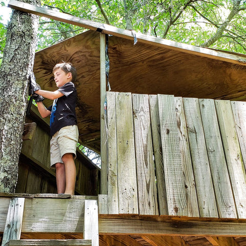 Child wearing gloves hammering in a treehouse