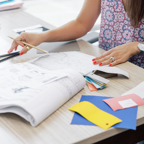 Women at desk holding pencil and looking at blueprints with color swatches nearby
