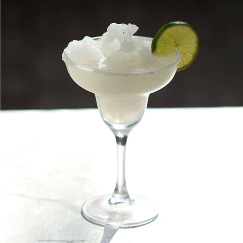 A classic frozen margarita with a lime slice on the glass rim, on a white counter