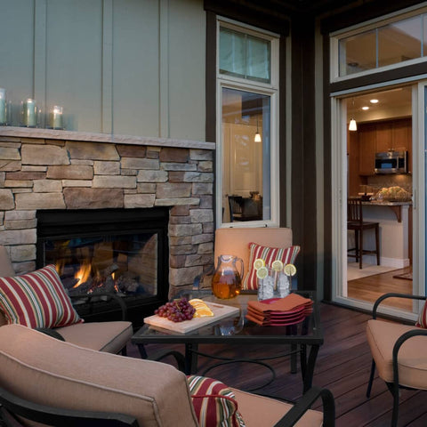 Metal chairs and coffee table on covered patio next to fireplace, with open door showing indoor kitchen