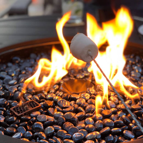 Firepit with charcoal and marshmallow on stick toasting above flames