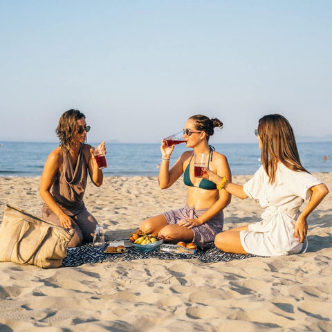Three woman sitting on the sand and drinking on the beach