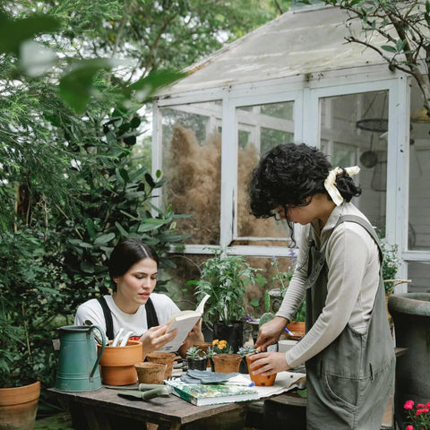 Two people at workstation with books, plants, and garden tools with a sunroom behind them