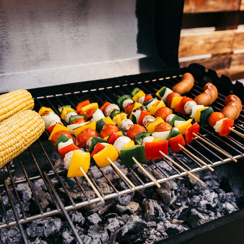 vegetable kabobs and corn on the cob resting on a charcoal grill