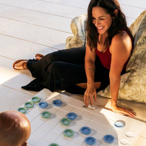 Woman lounging on the floor smiling while playing checkers