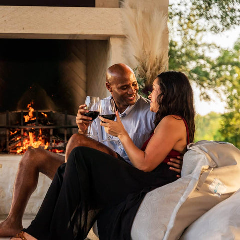 Couple sitting on cushions and drinking wine in front of outdoor fireplace