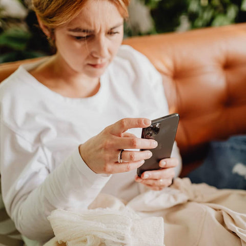 Woman sitting on leather couch looking stressed and tapping cell phone screen
