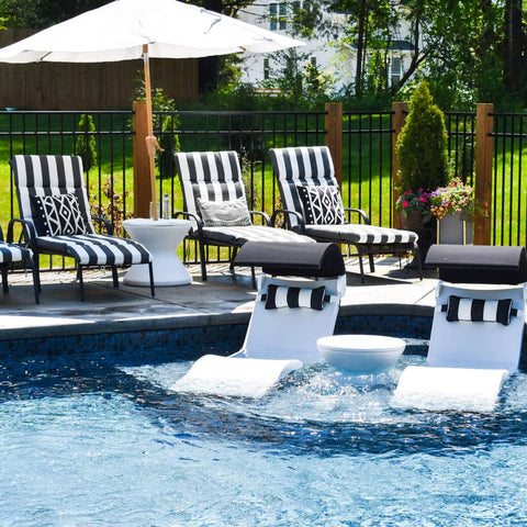 Chaises and side table on pool ledge, with lounge chairs, side table, and umbrella on patio next to pool