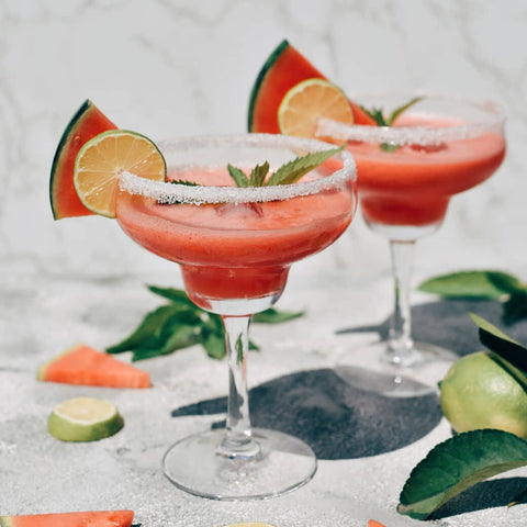 Two pink margaritas with lime, watermelon slices, and salt on the glass rim