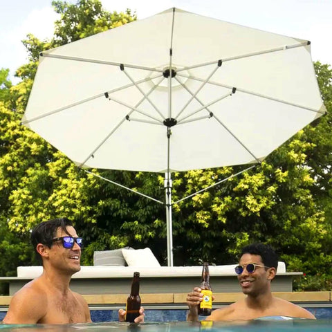 Two men in a pool holding beer bottles, in front of daybed and umbrella