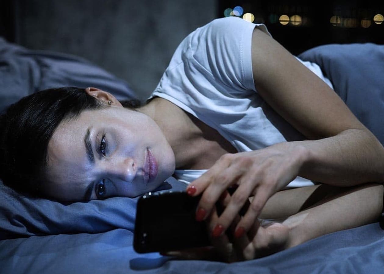 A woman laying in bed looking at her phone.
