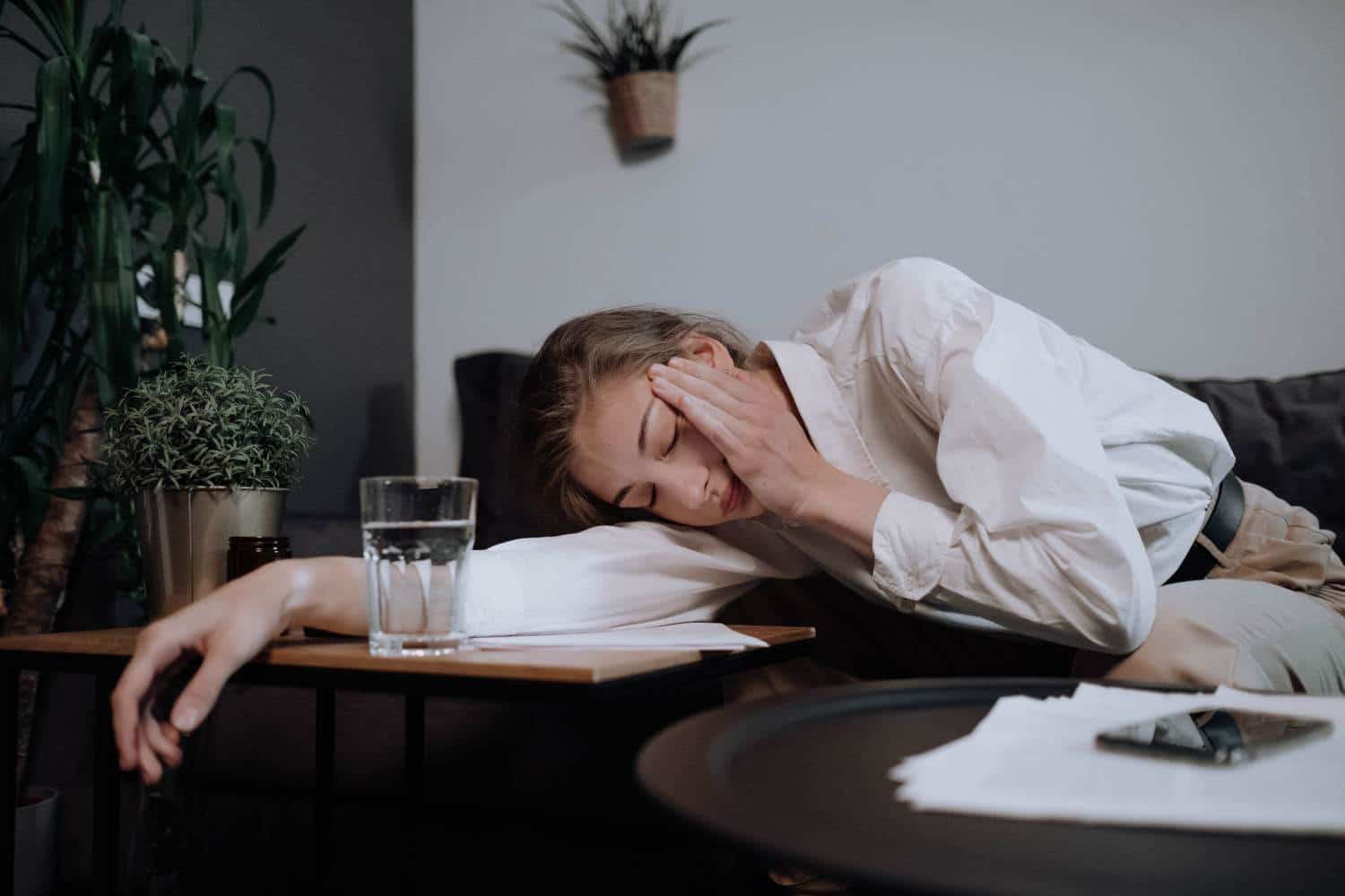 A woman is laying on a couch with her head on a glass of water.