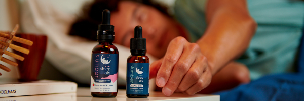 Two Slumber sleep aid bottles of cbn oil next to a person's bed.