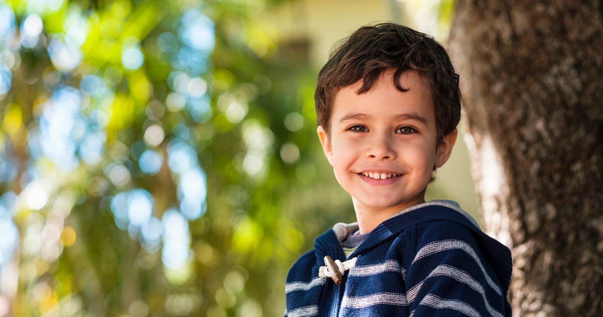 A smiling small boy sitting in a tree.