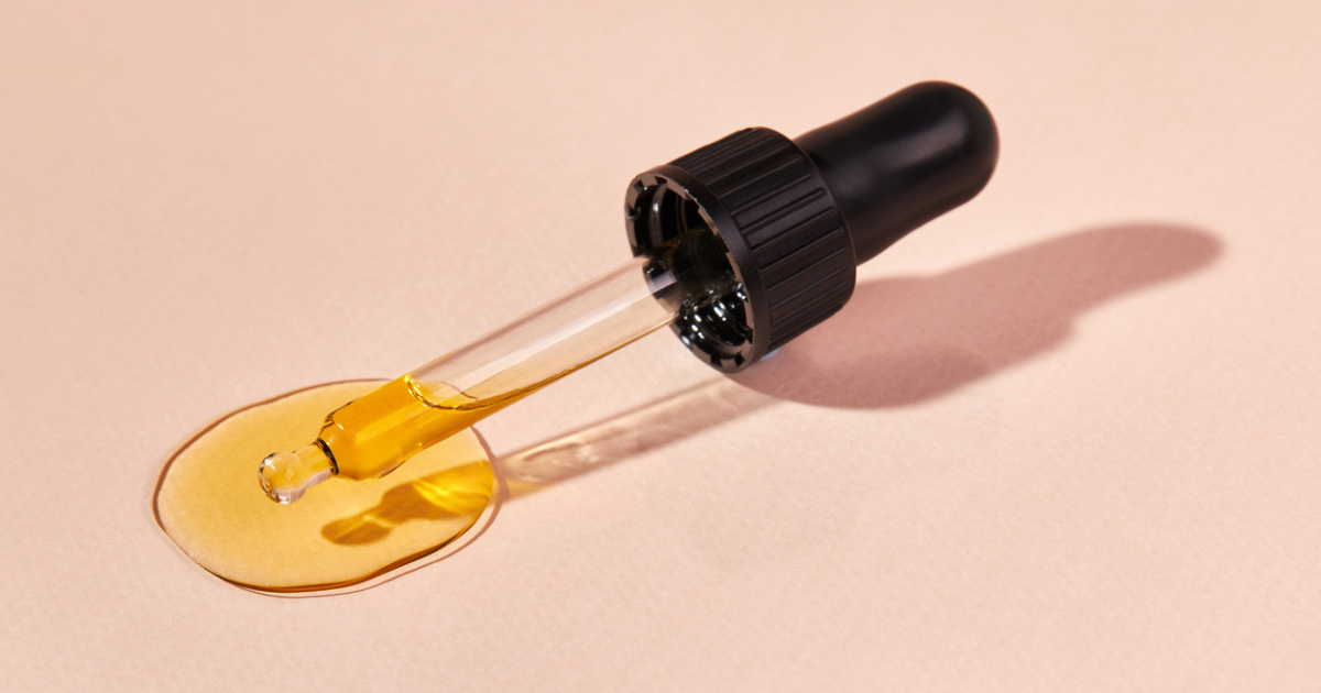 A glass oil pipette sitting a counter with a small amount of essential oil pooling at the bottom fo the tube.